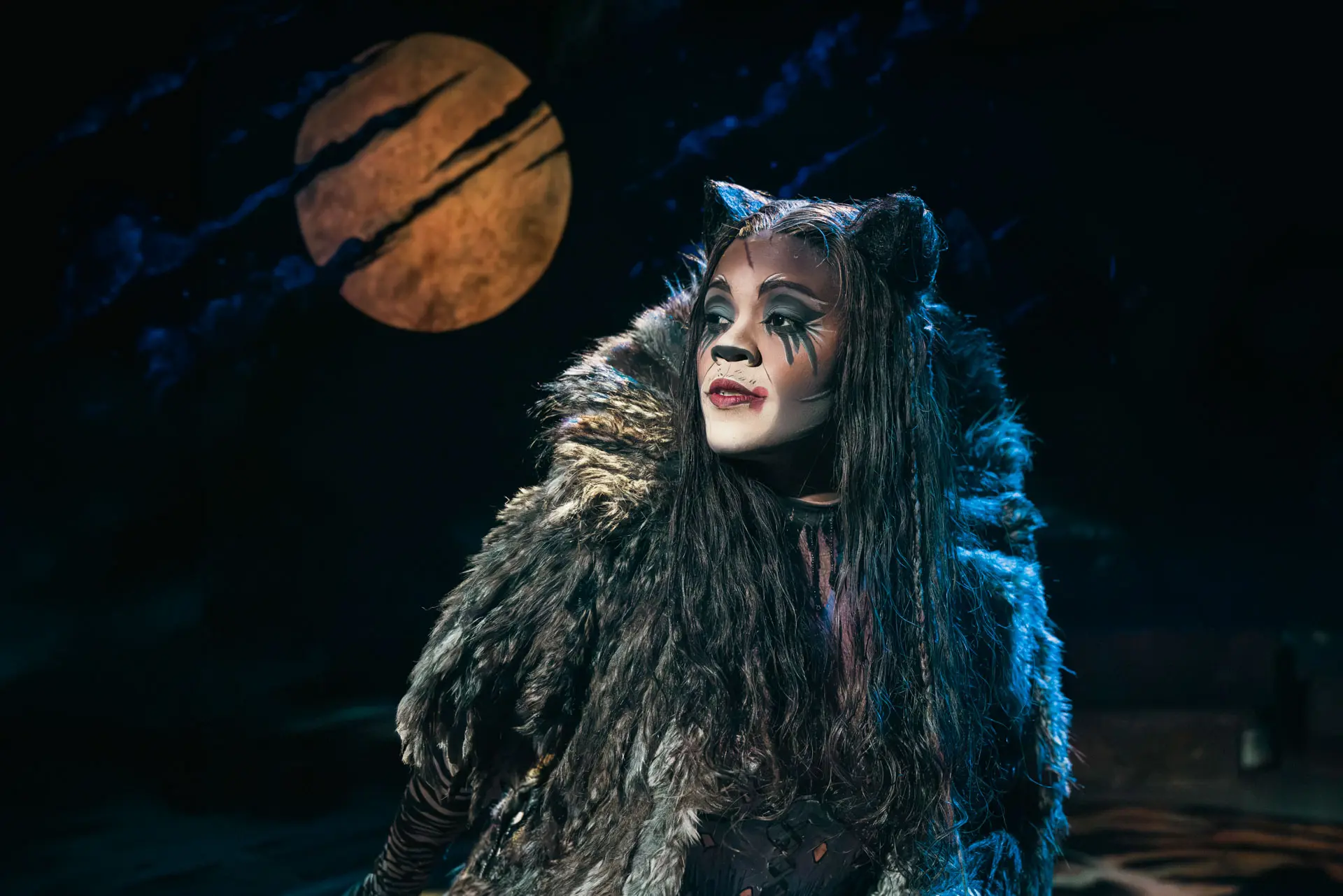 CATS The Musical – Cindy-Ann Abrahams as Grizabella, in a fur costume and cat make-up, gazing up beneath a full moon